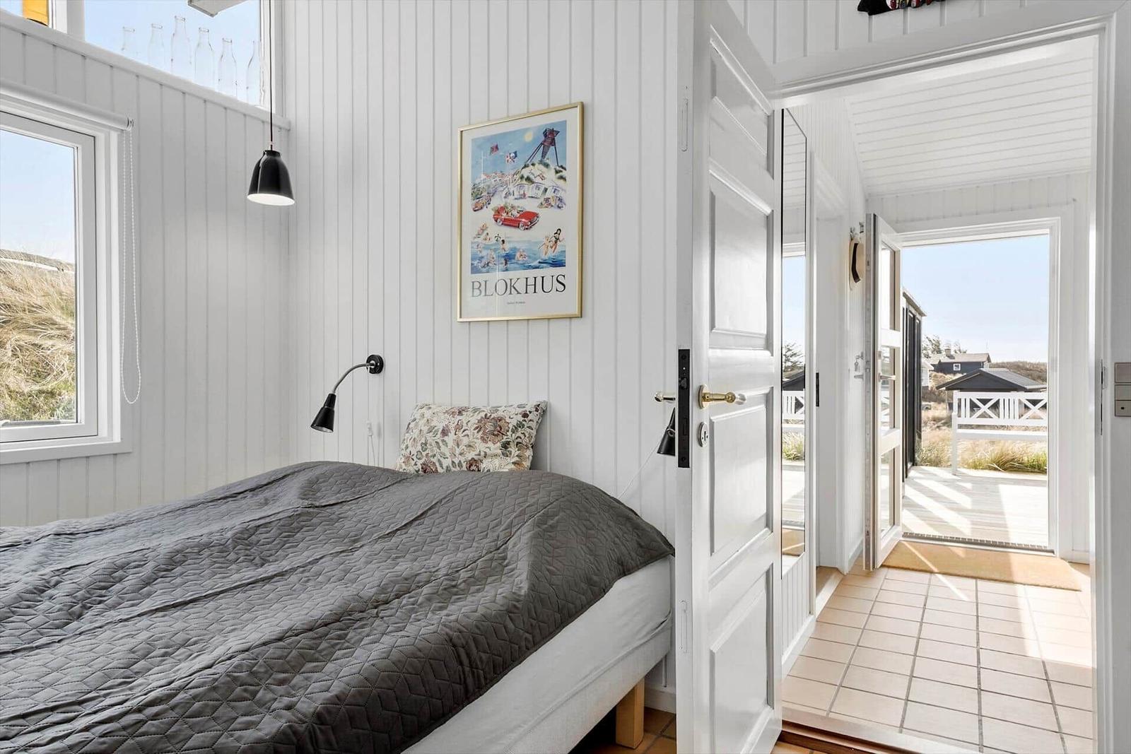Schlafzimmer mit Bett, Wandbild und Fenster. Tür führt zu Terrasse.