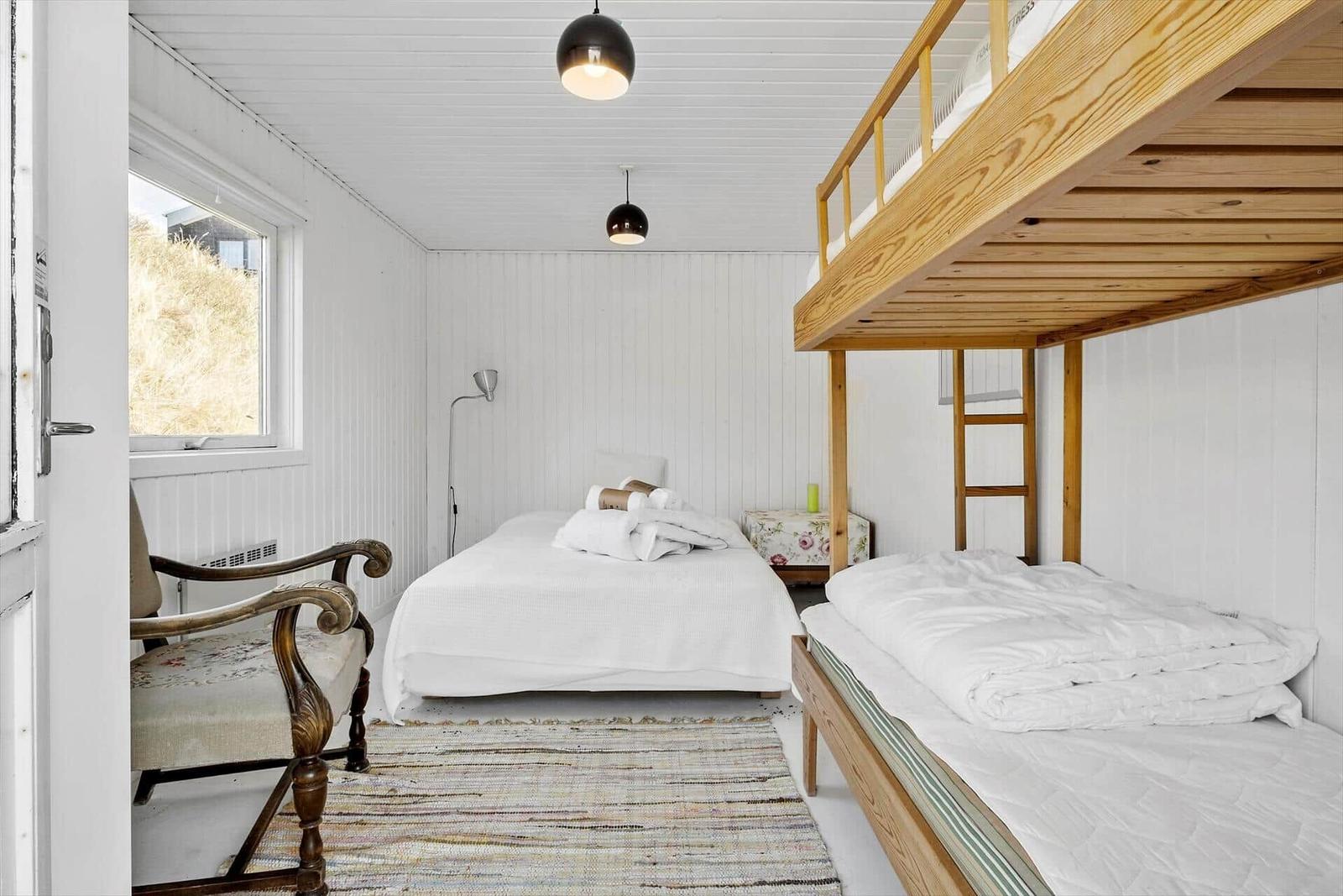 Schlafzimmer mit Doppelbett, Kletterbett und Sessel. Fenster mit Blick auf Gras.