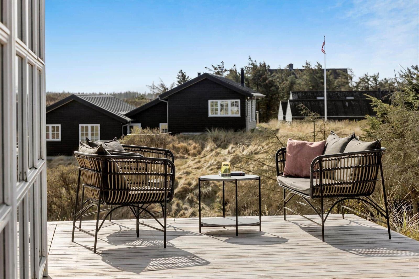 Terrasse mit zwei Sesseln und Tisch. Blick auf schwarze Häuser und Grasland.