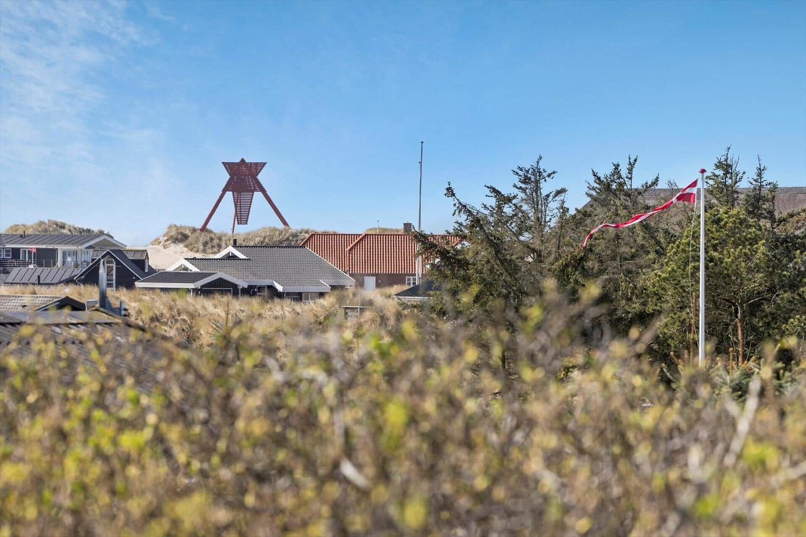 Dorf mit Häusern, roter Skulptur und dänischer Flagge unter blauem Himmel.