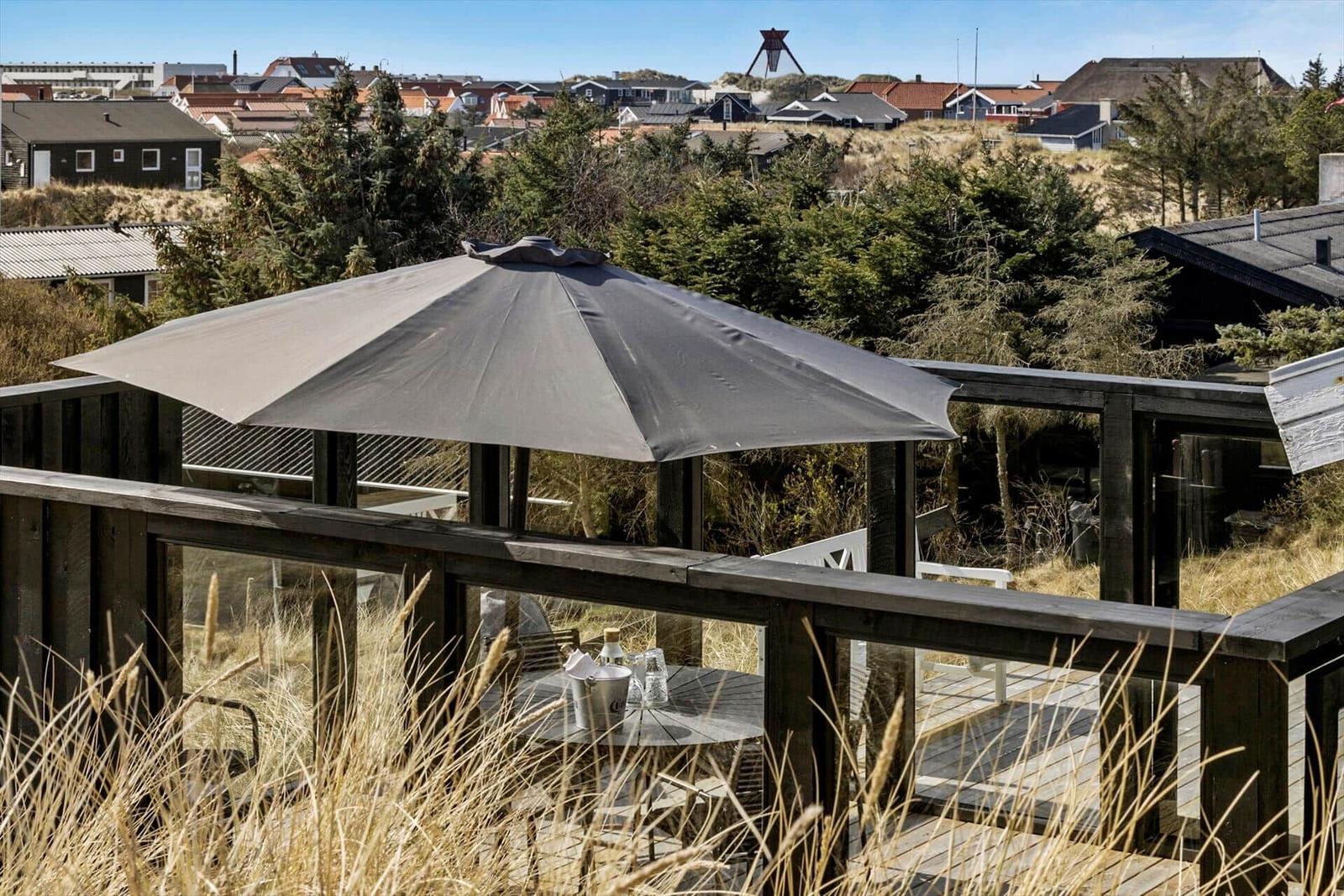 Terrasse mit Sonnenschirm und Tisch. Blick auf Dörfer und Bäume.