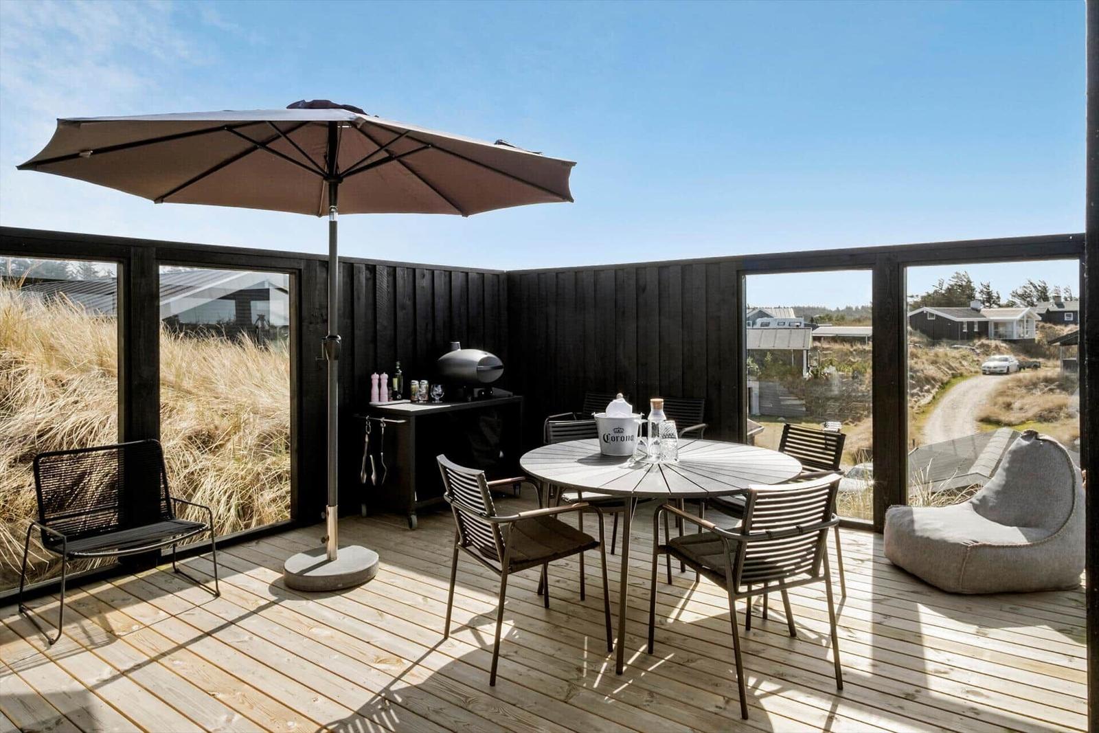 Terrasse mit Tisch, Stühlen, Sonnenschirm und Grill. Blick auf Gras und Häuser.