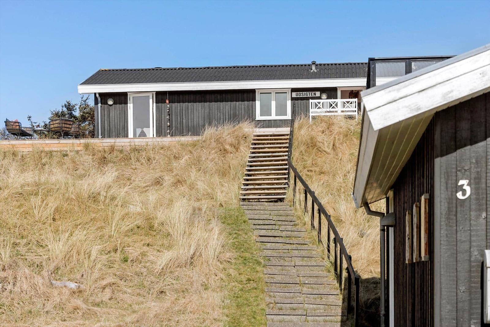 Haus mit Holzterrasse und Stufen durch Grasland. Schild mit Aufschrift UDSIGTEN.
