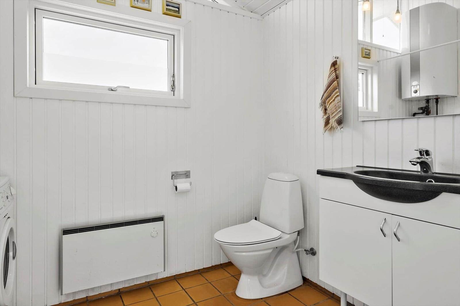 Badezimmer mit Toilette, Waschbecken und Fenster. Weiße Wände, brauner Boden und Spiegel.