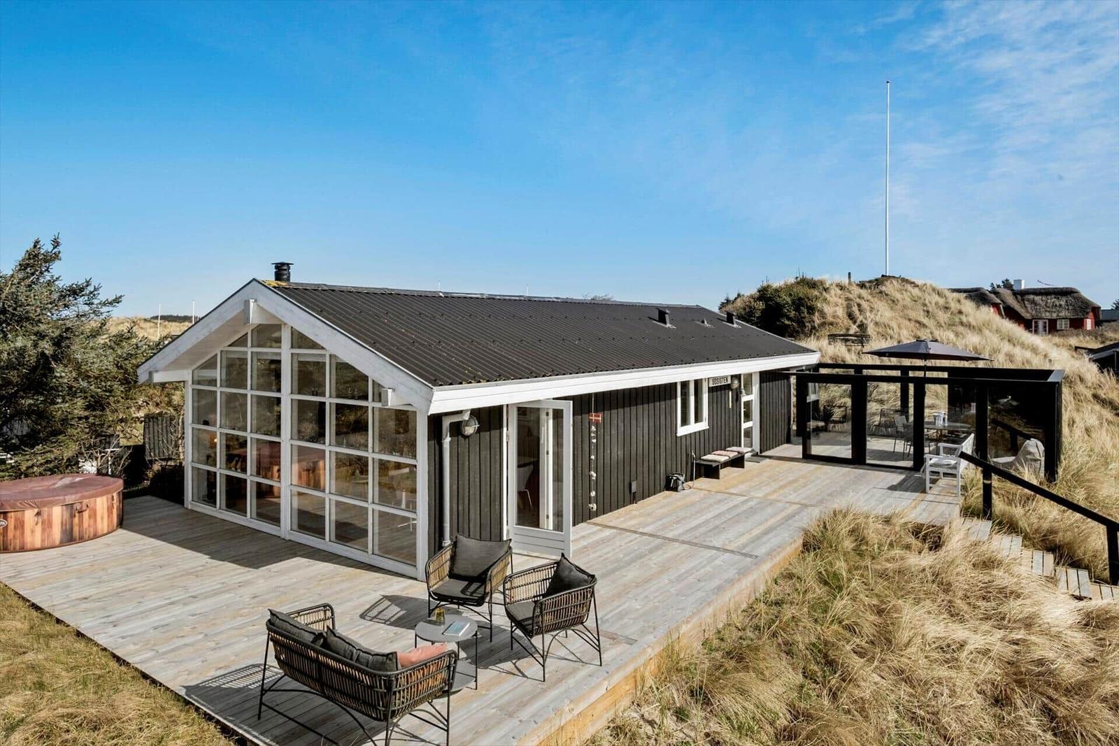 Moderne Villa mit Terrasse, Whirlpool und Sitzgelegenheiten in einer grünen Umgebung.