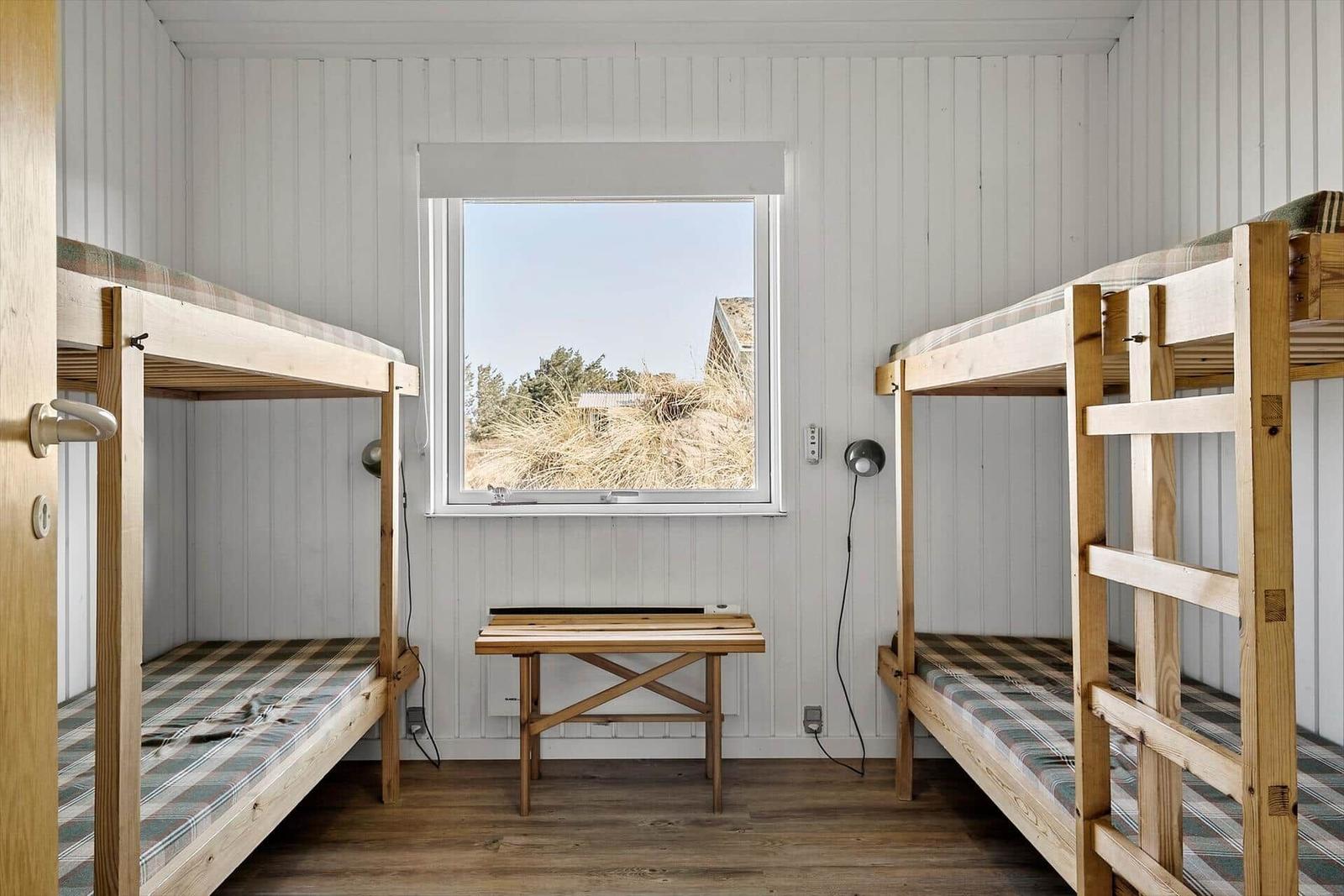 Zwei Etagenbetten mit Tisch und Fensterblick auf Gras.