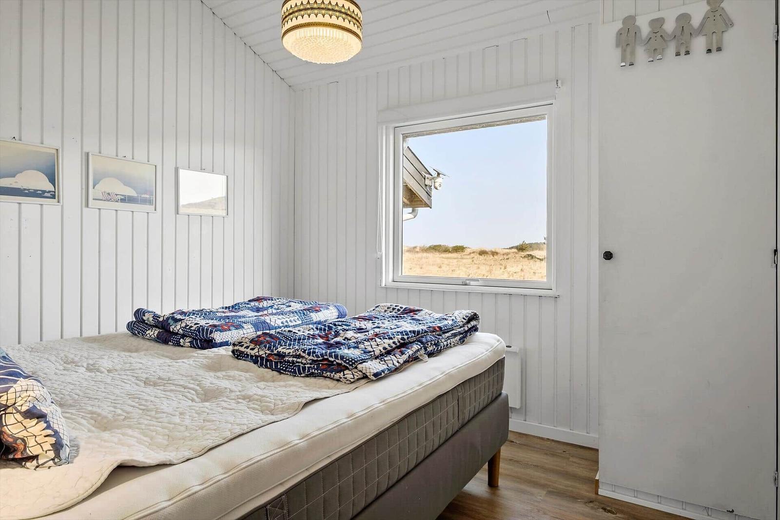 Schlafzimmer mit Bett, Fenster und Wandbildern.