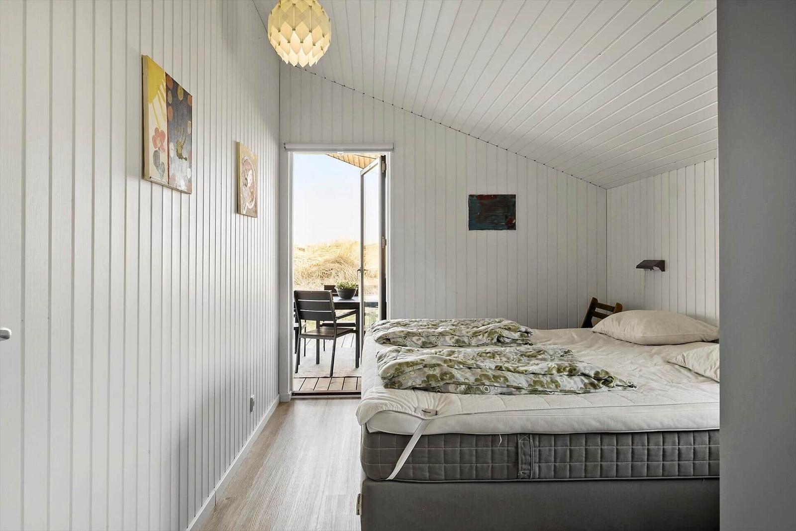 Schlafzimmer mit Bett, Fenster und Wandbildern.