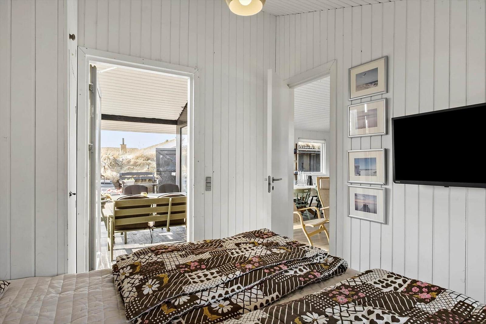 Schlafzimmer mit Bett, Fernseher und Blick auf Terrasse.