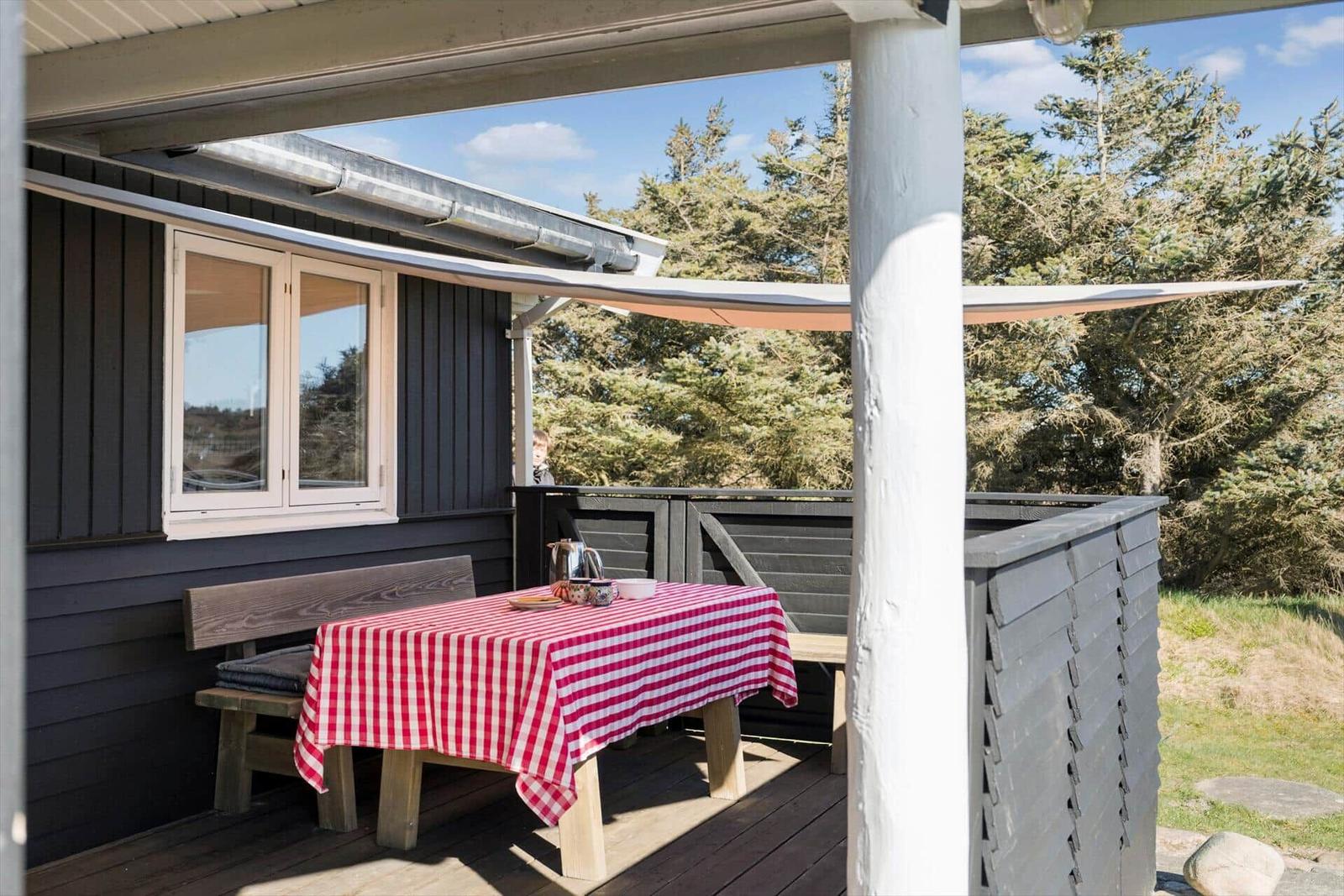 Terrasse mit Tisch, rotem Tischtuch und Bänken. Hintergrund: Wald und Himmel.