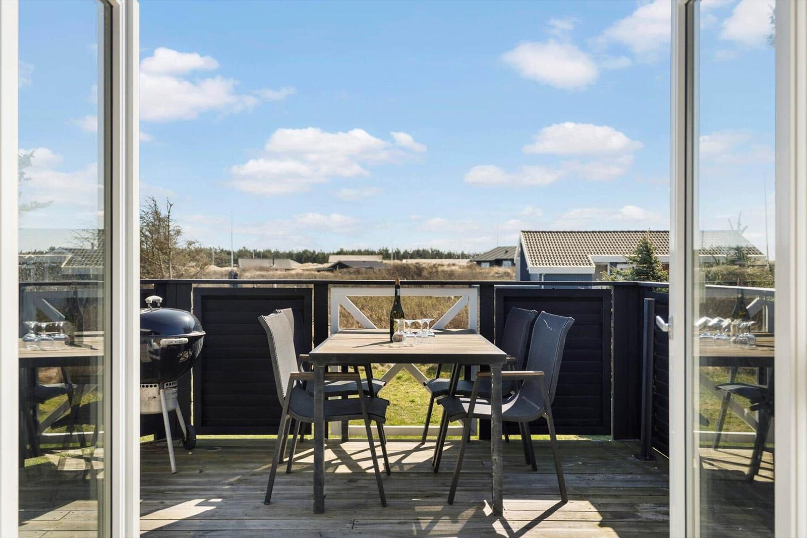 Terrasse mit Tisch, Stühlen und Grill. Blick auf Gras und Häuser.