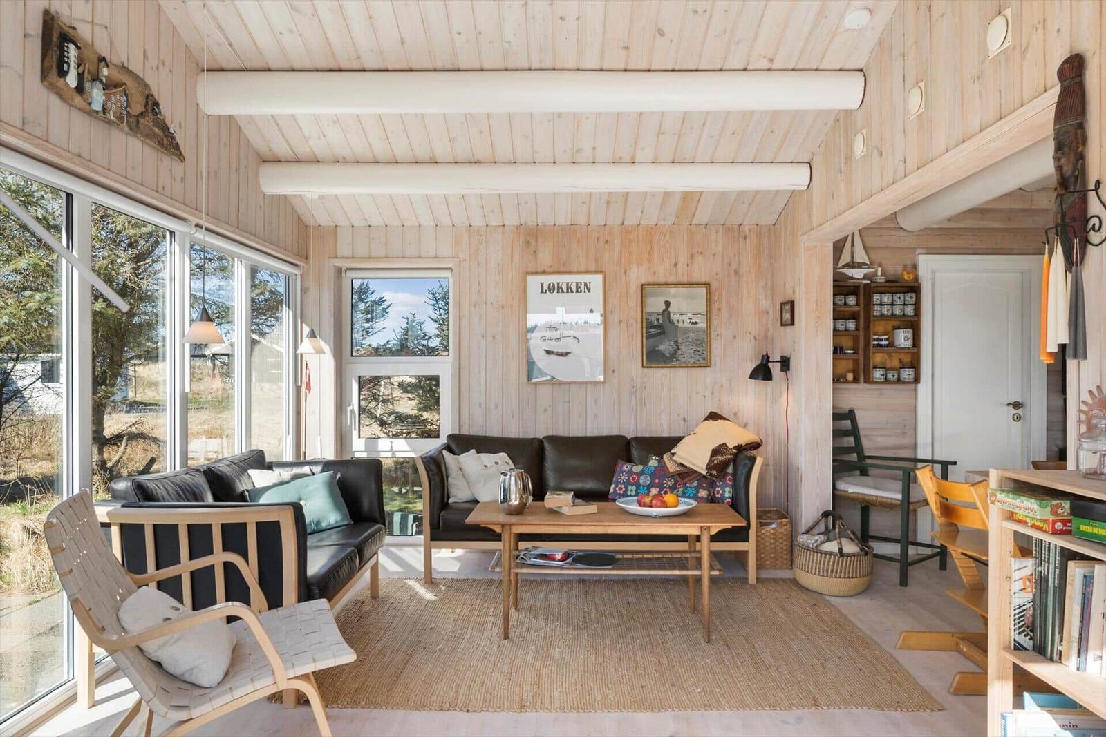 Wohnzimmer mit Holzwand, Sofa, Tisch und Fenstern.