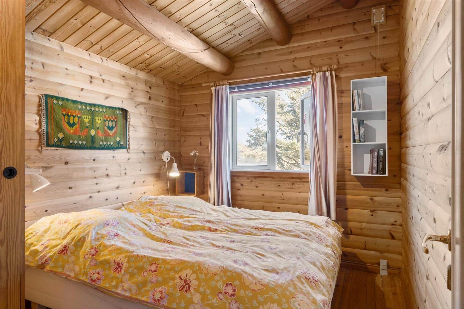 Schlafzimmer mit Holzwand, Bett und Fenster mit Blick auf Bäume.