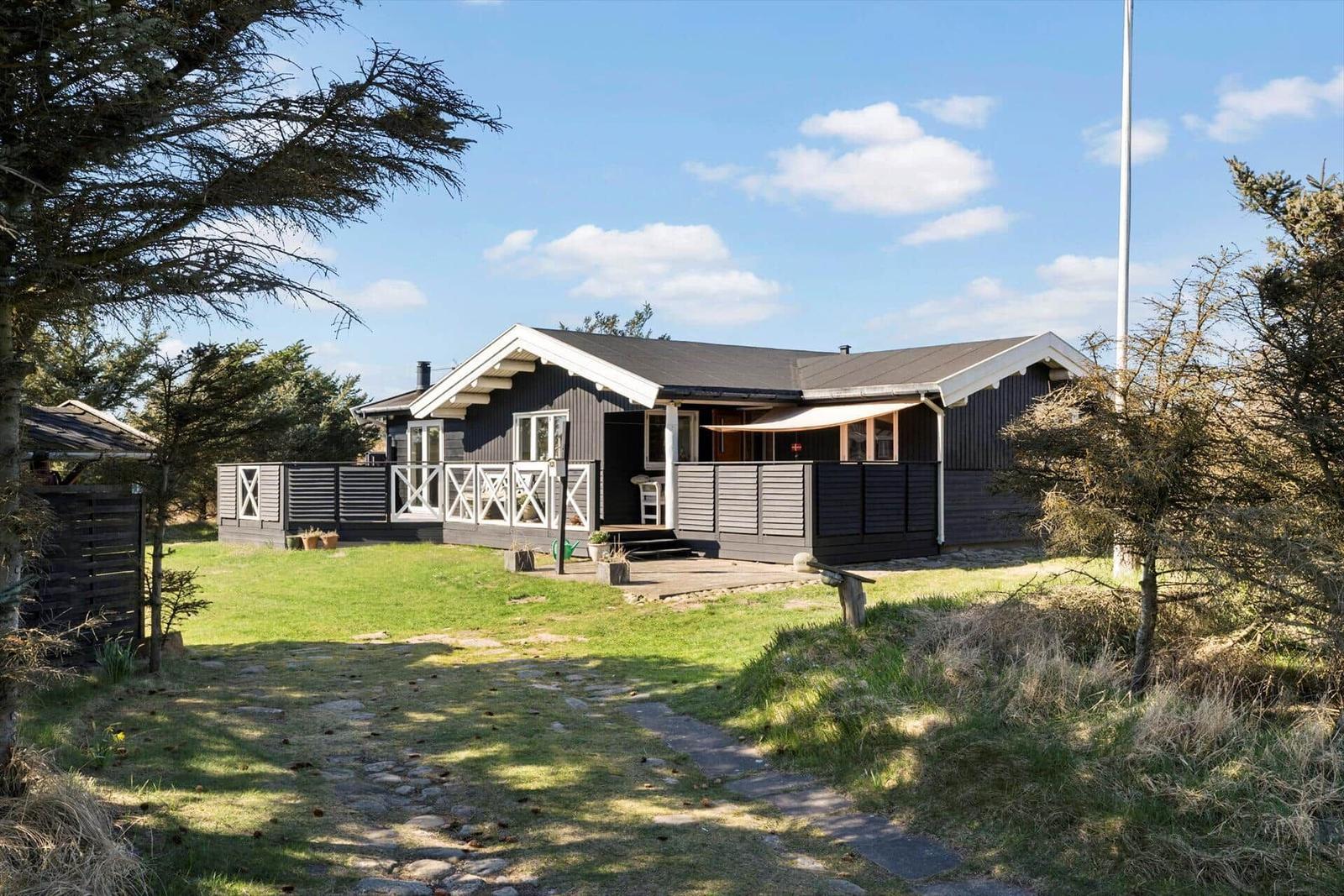 Ein dunkel gestrichenes Ferienhaus mit Terrasse und Garten unter blauem Himmel.
