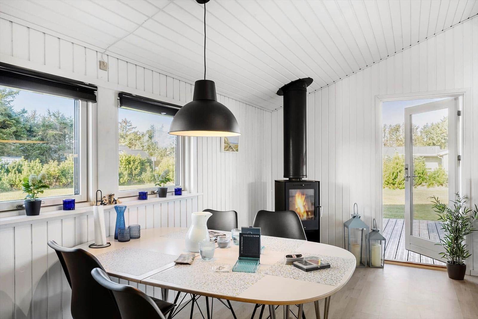 Dining room with table, chairs, and wood stove. Windows and door show garden.