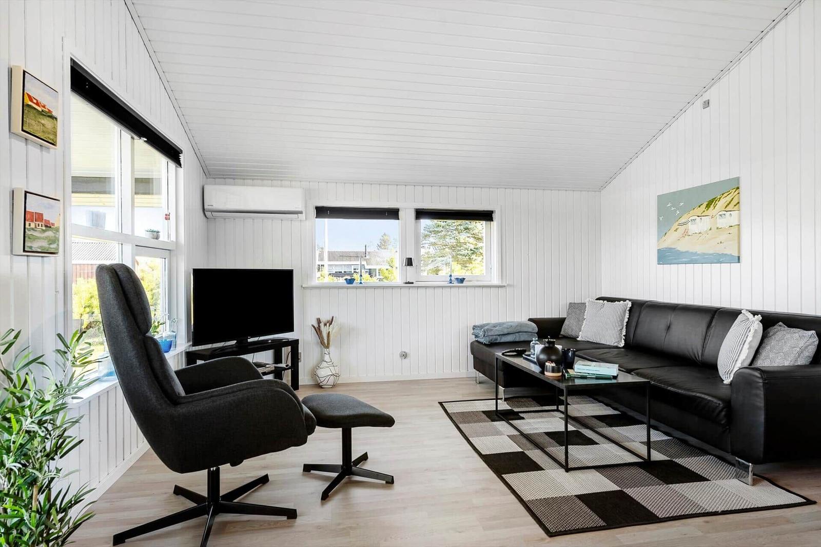 Living room with sofa, chair, and TV. White walls and wooden floor.