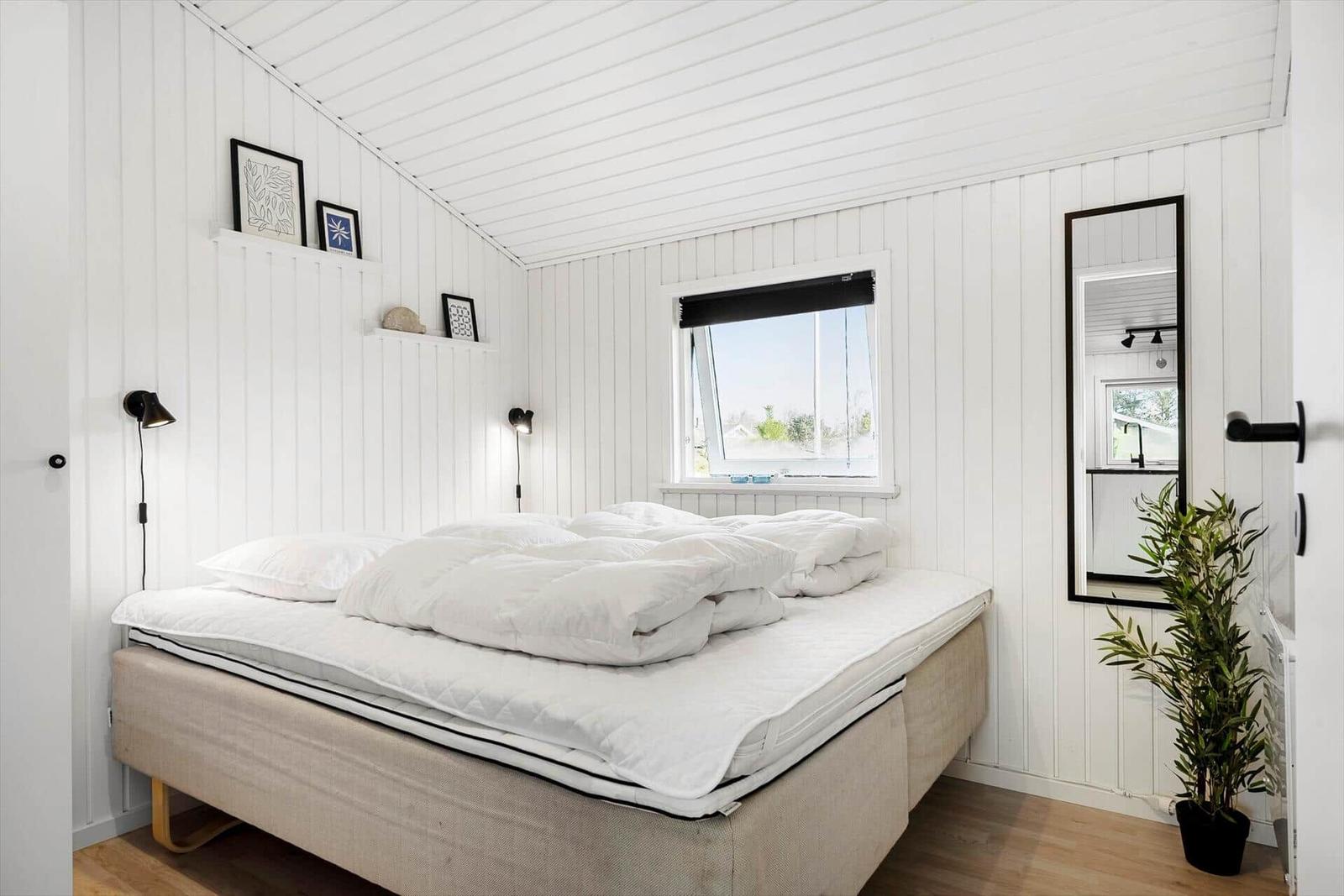 Bedroom with white bed, window, and mirror on the wall.