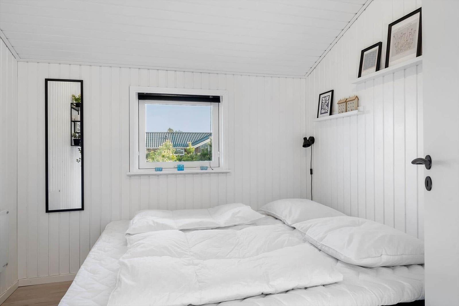 Bedroom with white wood walls, bed, and window view.