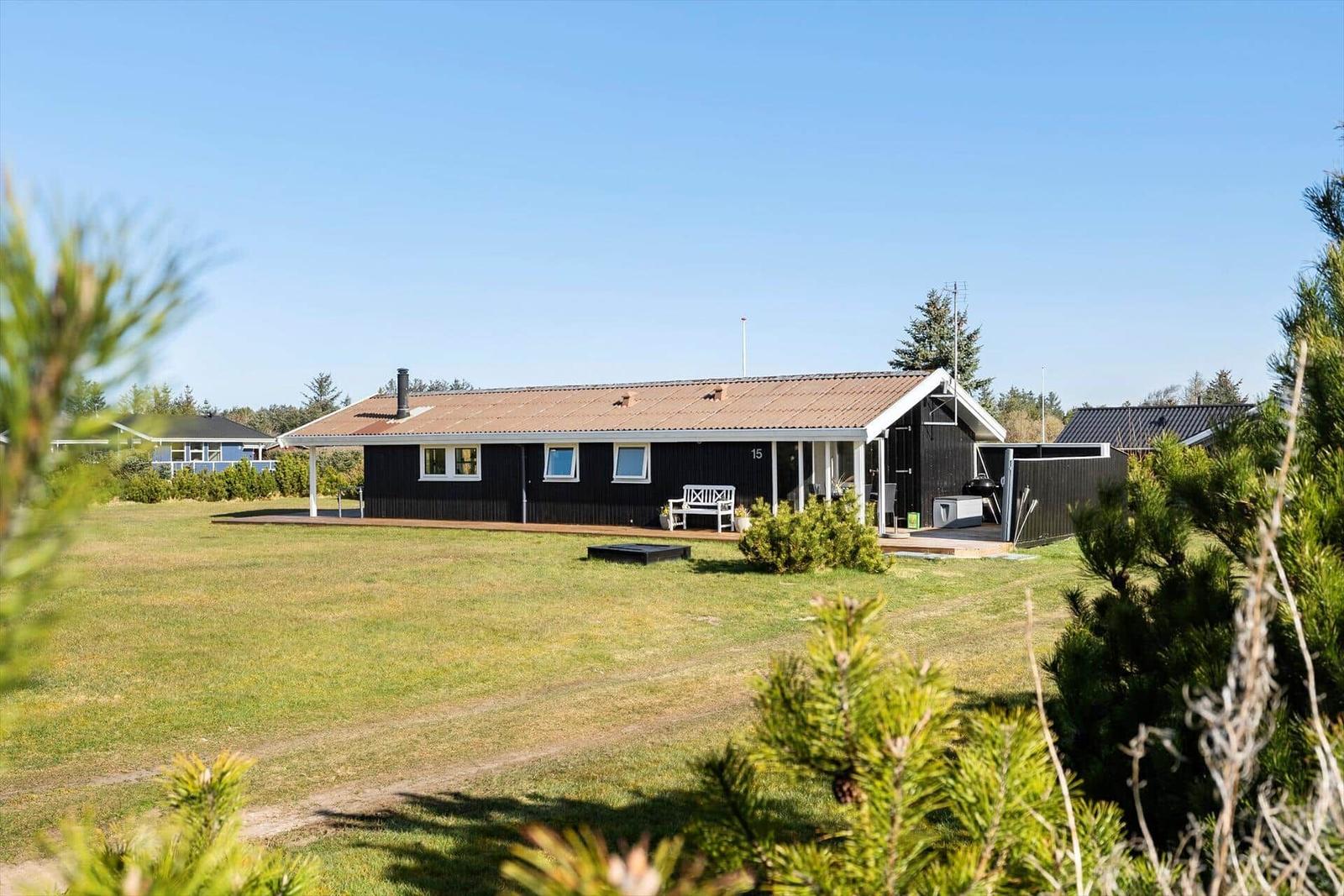 Black holiday house with terrace and garden. House number 15. White bench and grill in the outdoor area.