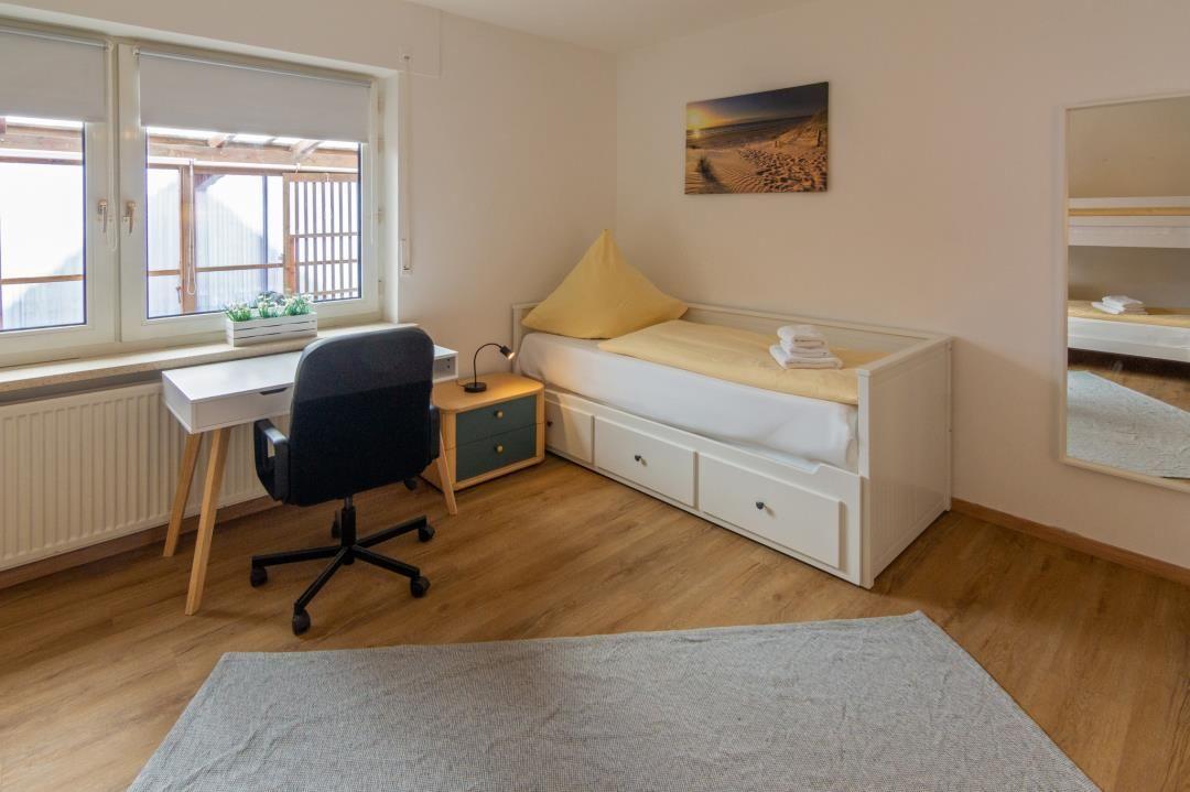 Schlafzimmer mit Bett, Schreibtisch und Fenster. Spiegel und Wandbild sichtbar.