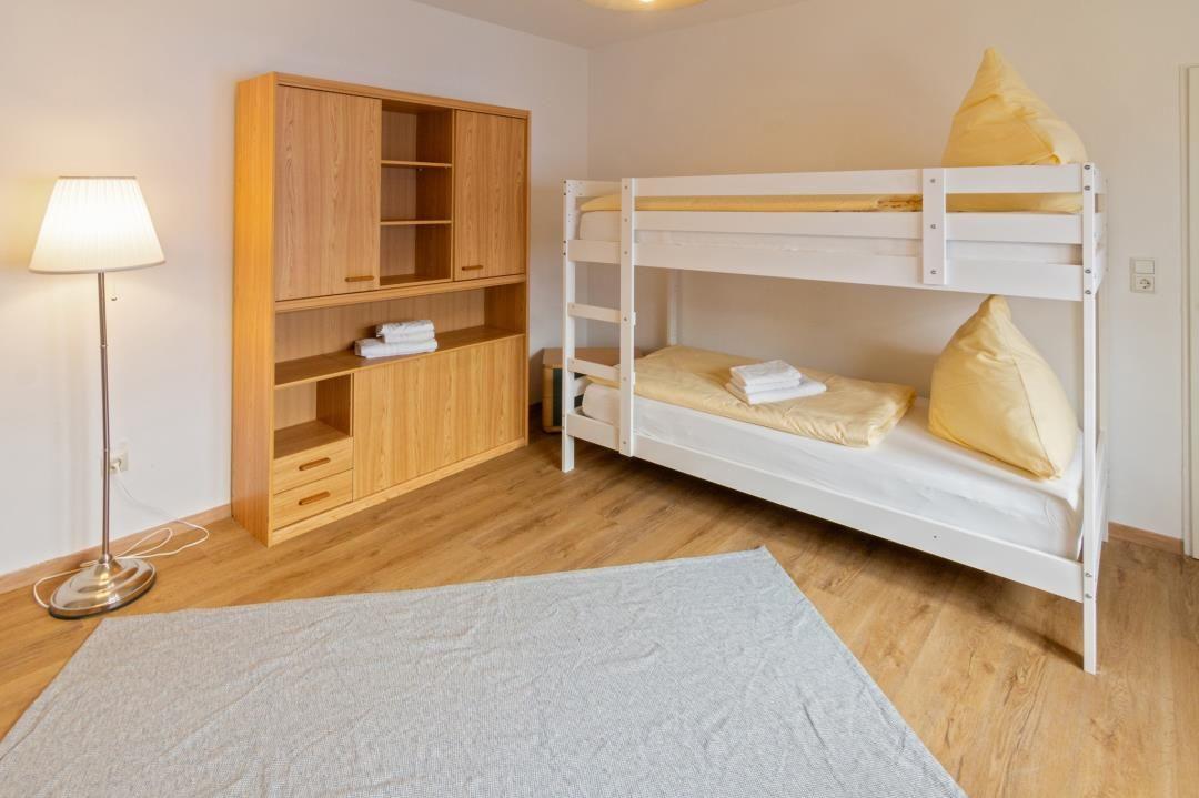 Zimmer mit Doppelstockbett, Holzschrank und Stehlampe auf Holzboden.