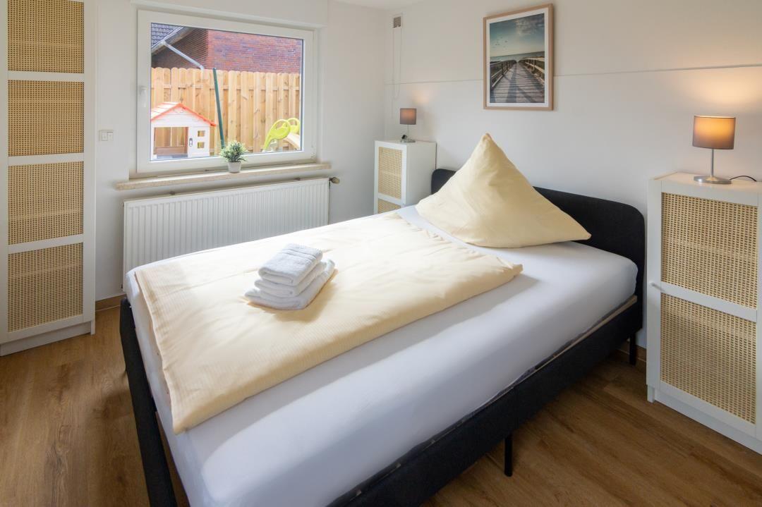 Schlafzimmer mit Bett, Nachttisch und Fensterblick auf Garten.