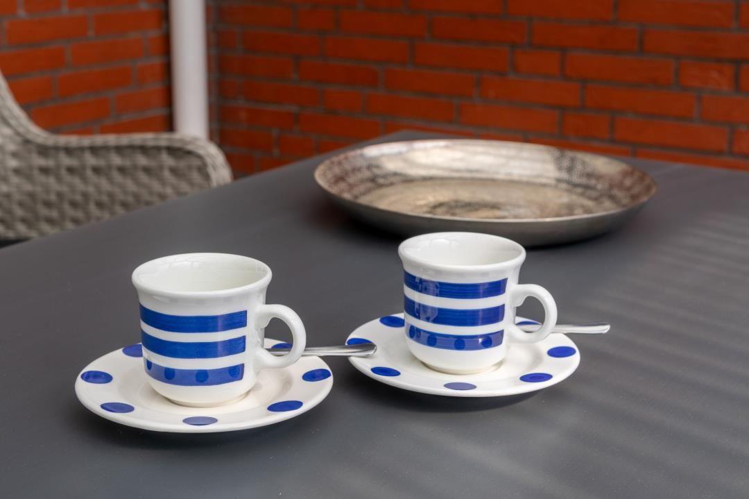 Zwei Tassen mit blauen Streifen stehen auf Untertassen auf einem Tisch.