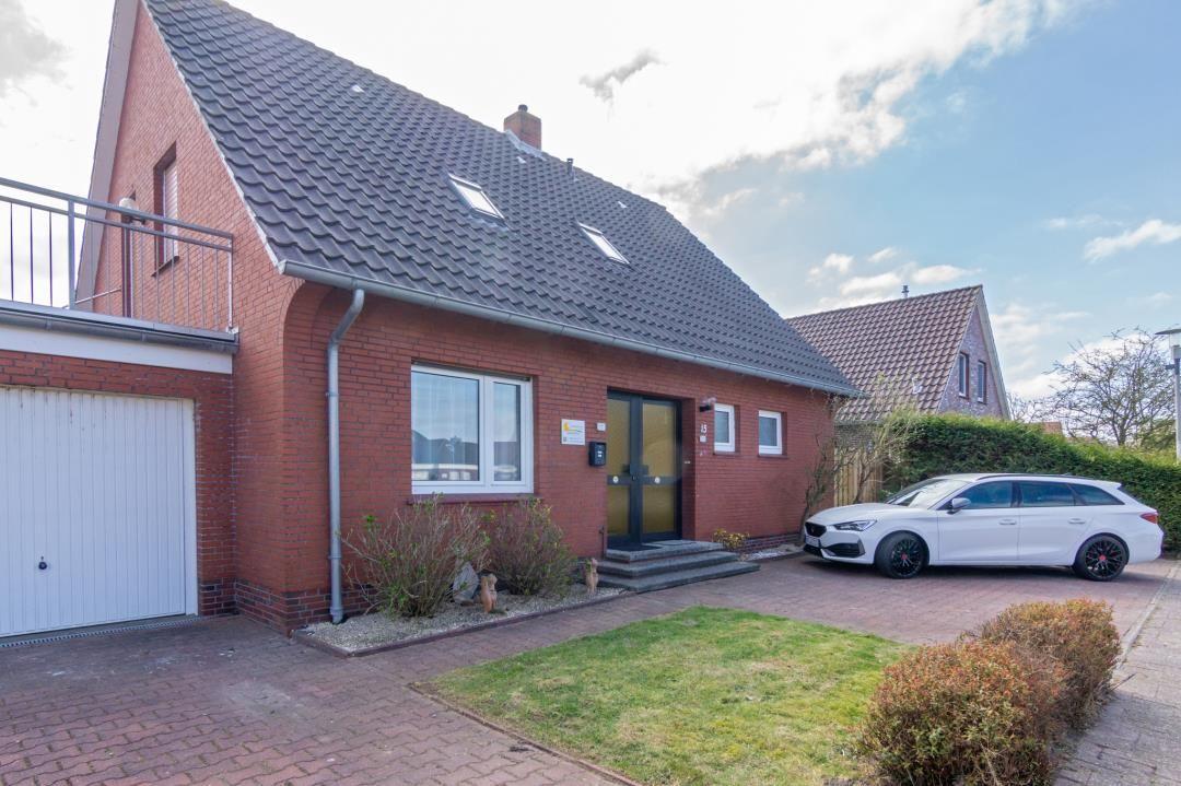 Rotes Backsteingebäude mit Garage und gepflasterter Hof. Ein Auto steht vor dem Haus.