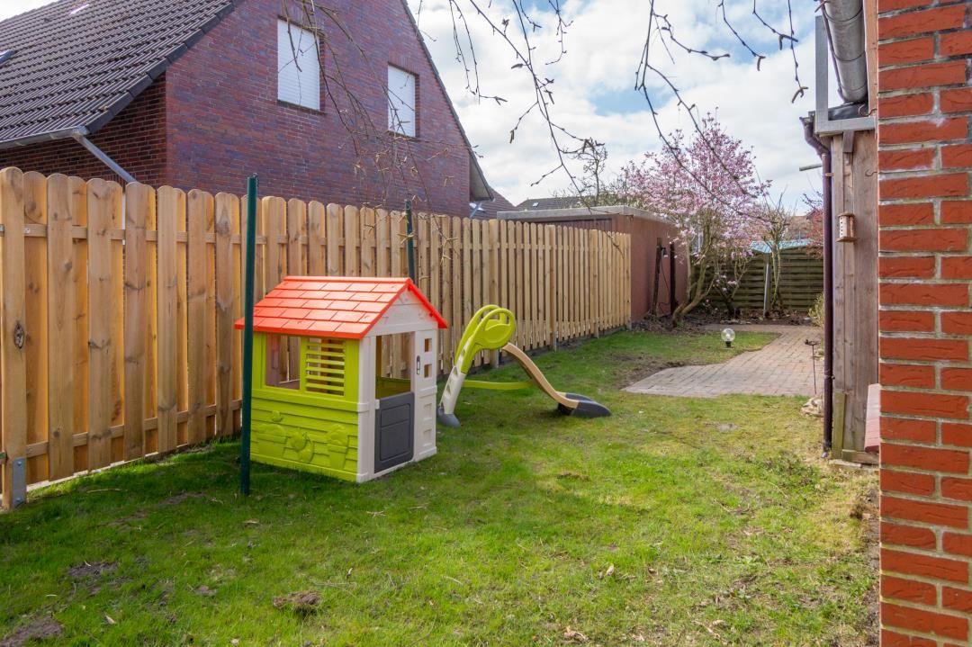 Hinterhof mit Spielhaus und Rutsche, umzäunt und grün.