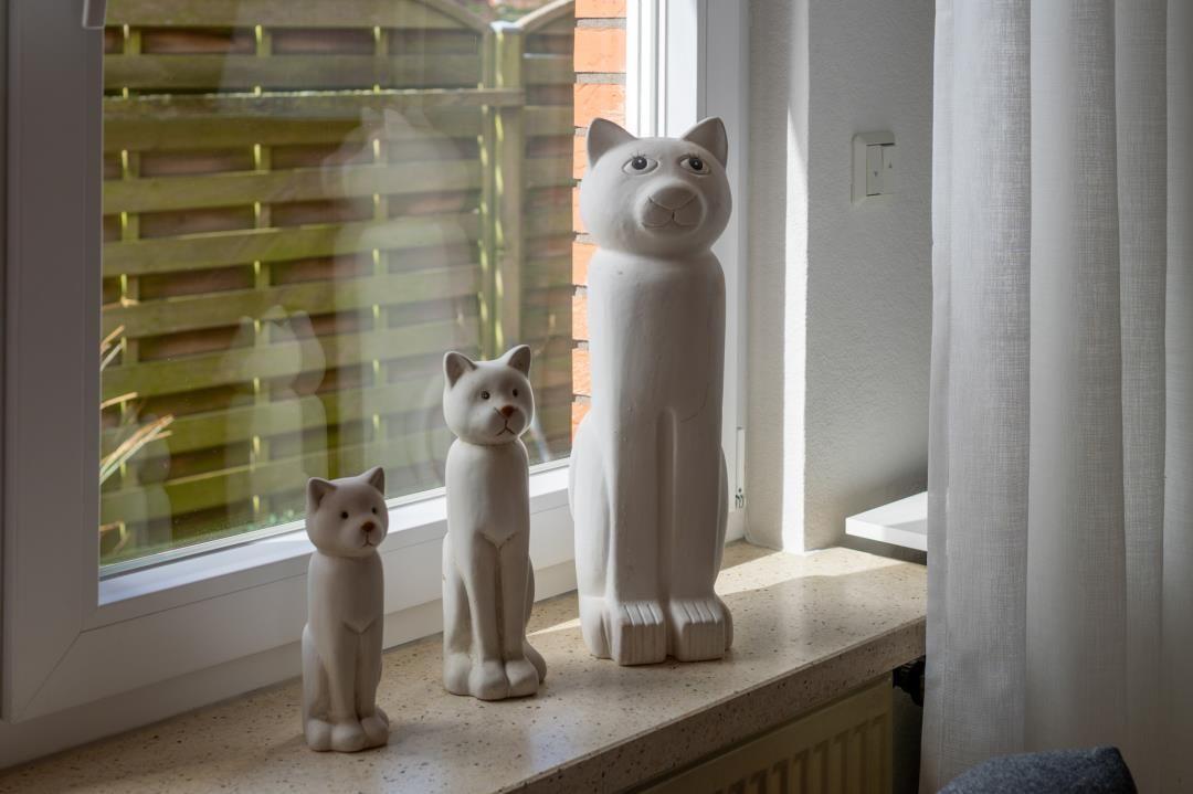 Drei weiße Katzenfiguren stehen auf einem Fensterbrett.