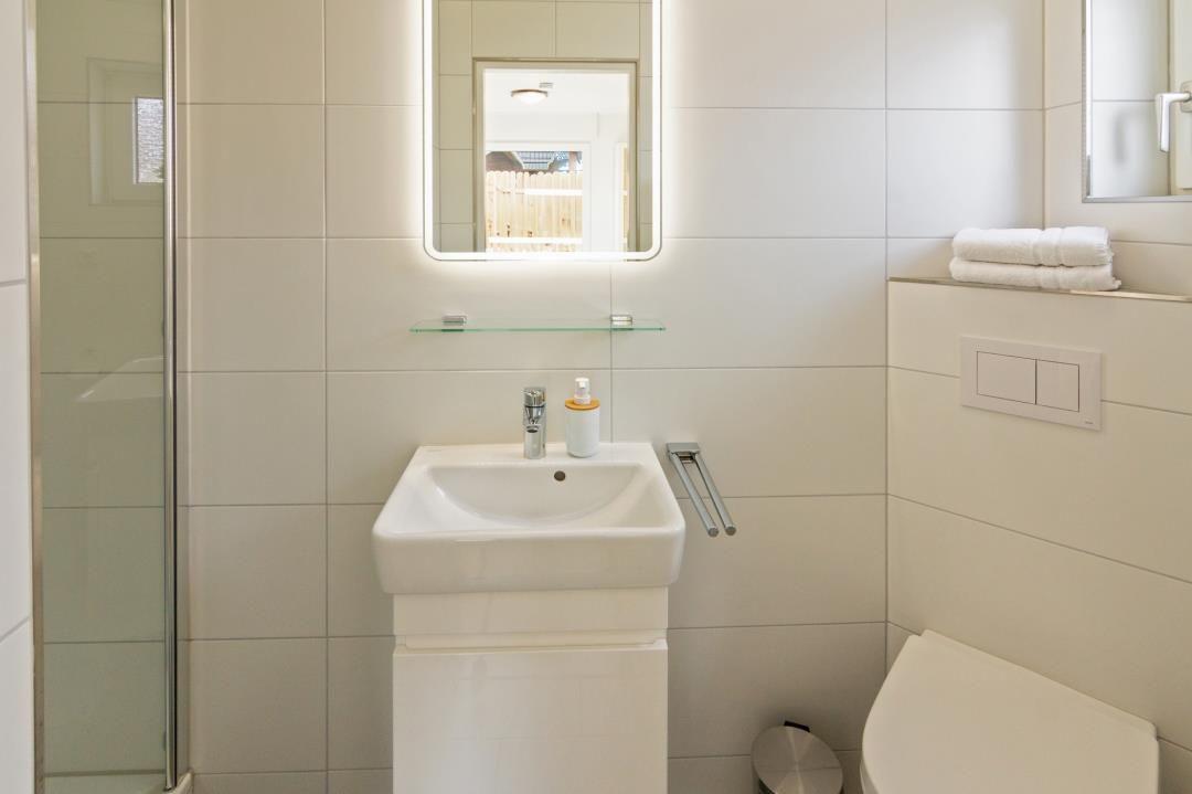 Badezimmer mit Waschbecken, Spiegel, Dusche und Toilette.