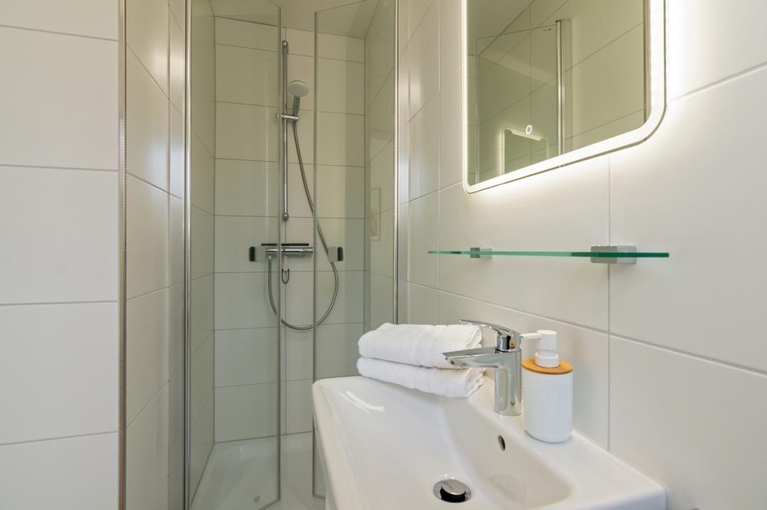 Badezimmer mit Dusche, Waschbecken und beleuchtetem Spiegel.