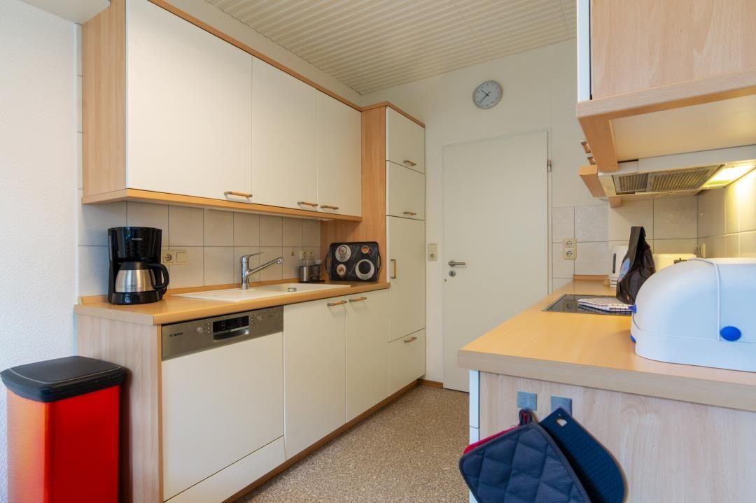 Küche mit weißen Schränken, Spüle, Kaffeemaschine und Dunstabzug.