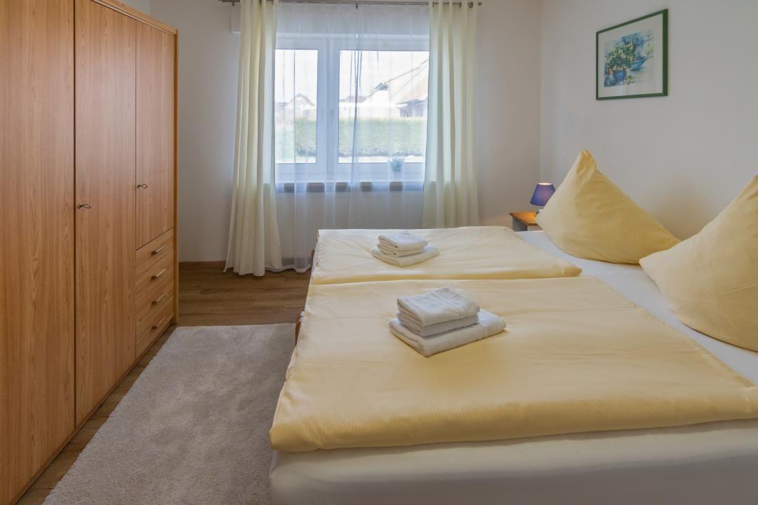 Schlafzimmer mit Doppelbett, Kleiderschrank und Fenster mit Vorhängen.