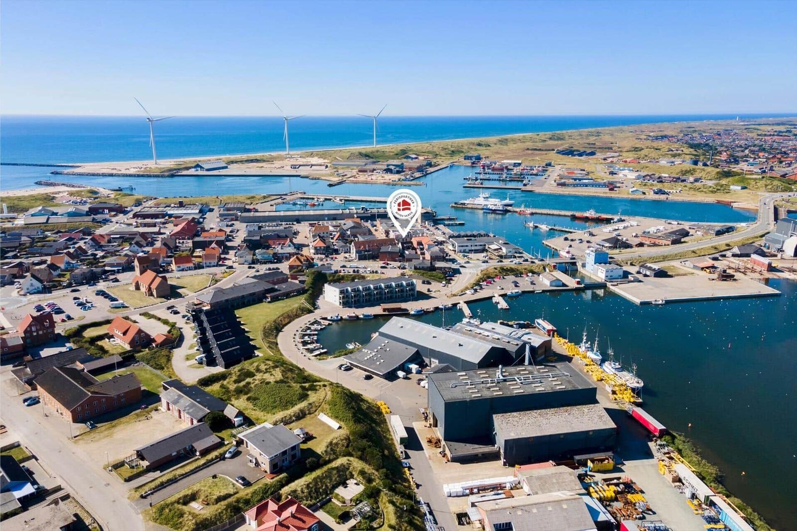 Aerial view of a harbor town with wind turbines, boats, and buildings near the sea.