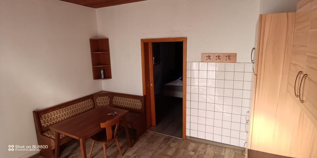 Essbereich mit Holztisch und Bänken. Tür führt in Schlafzimmer. Küchenwand mit Fliesen.