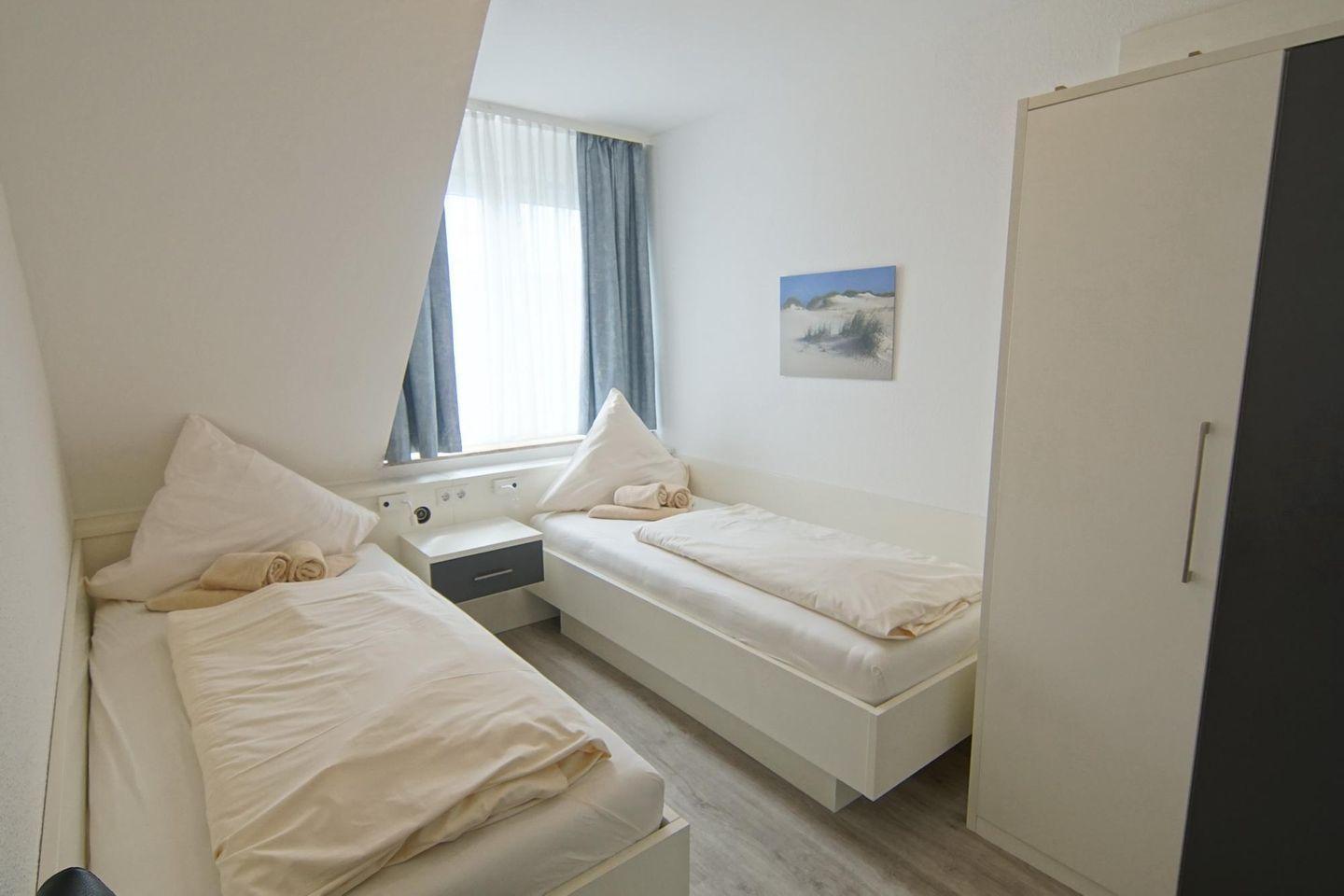 Zwei Einzelbetten, Fenster, Kleiderschrank und Wandbild in einem Zimmer.