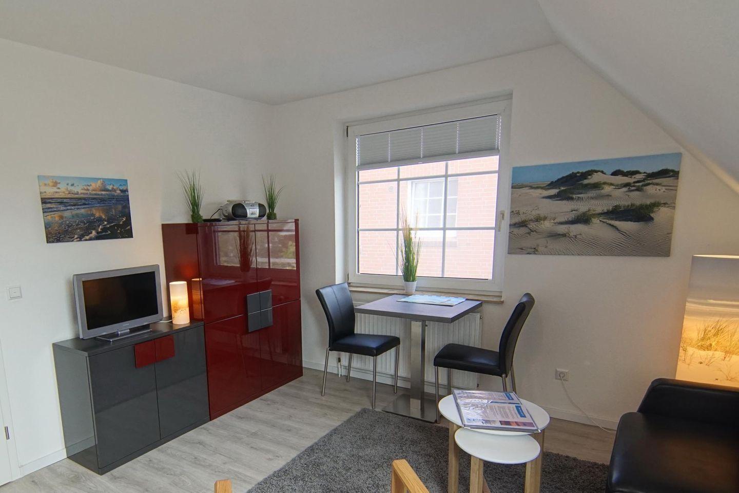 Wohnzimmer mit TV, Tisch, Stühlen und Wandbildern