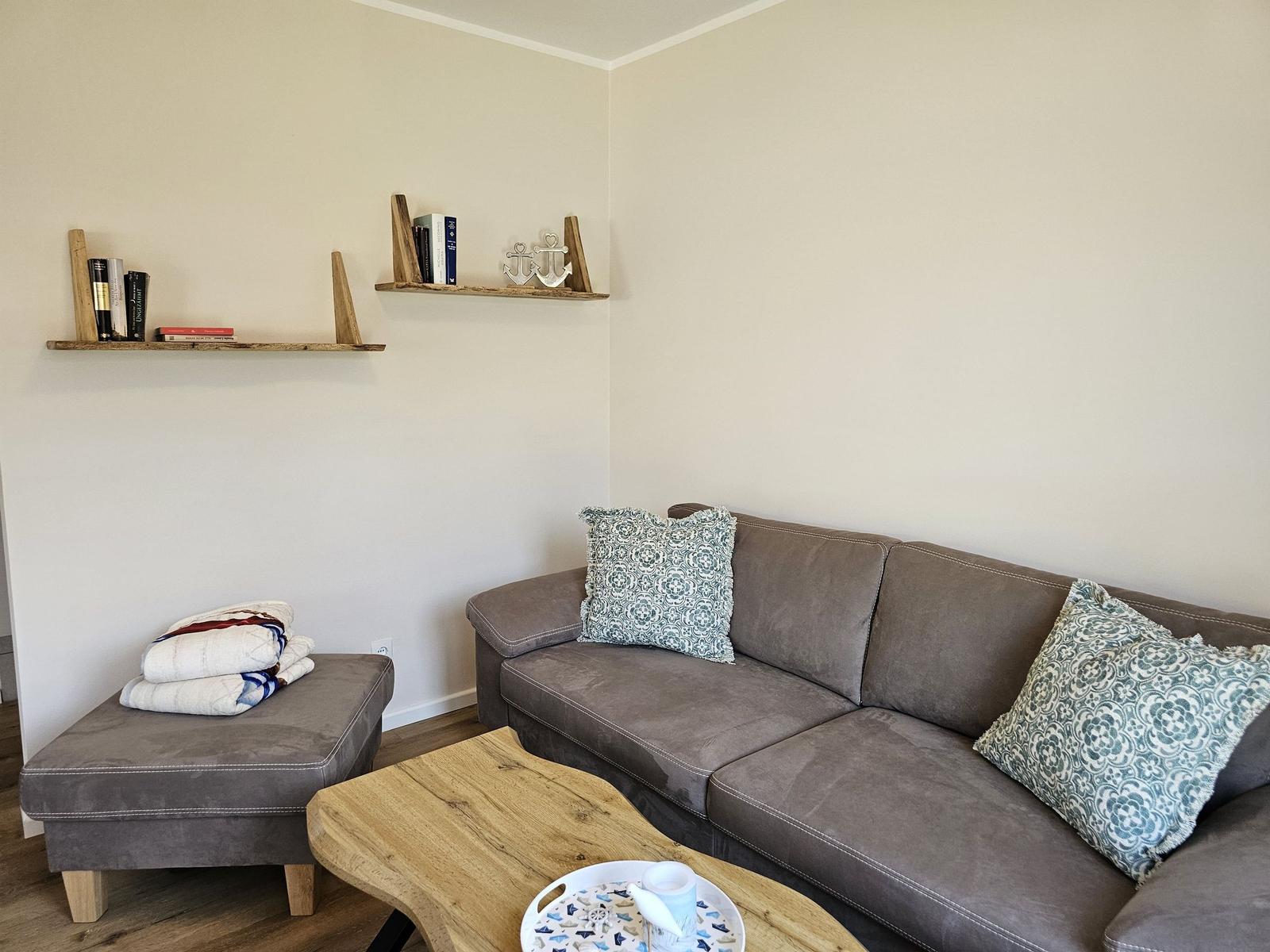 Ein Wohnzimmer mit Sofa, Kissen, Holztisch und Regalen an der Wand.