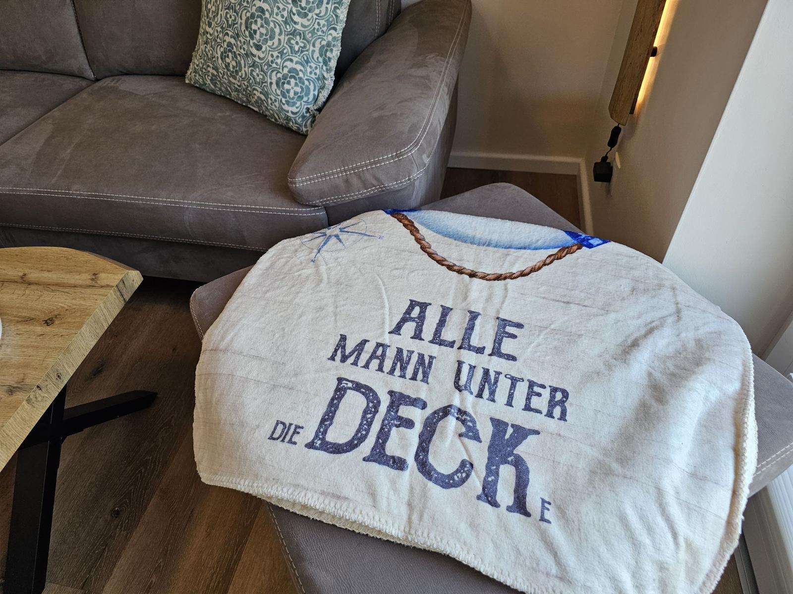 Ein grauer Sofa mit Kissen und ein Decke mit Aufschrift.