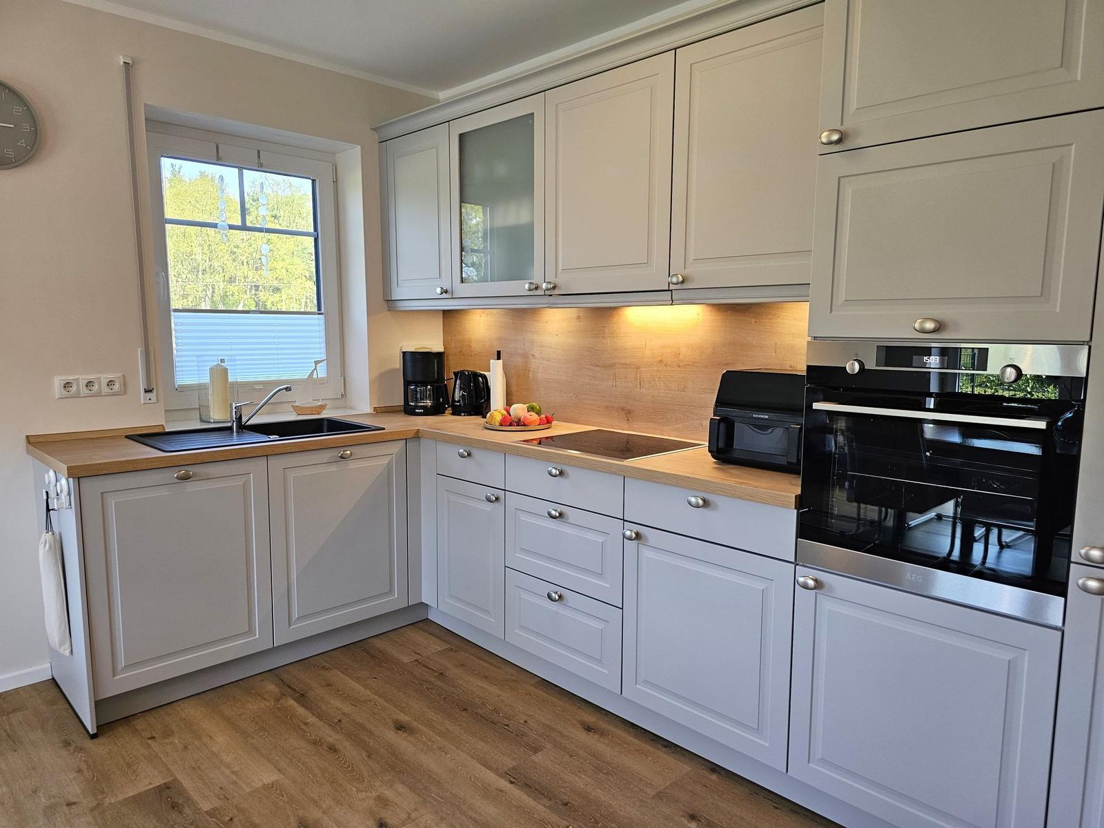 Küche mit hellen Schränken, Holzoberflächen und integriertem Backofen.