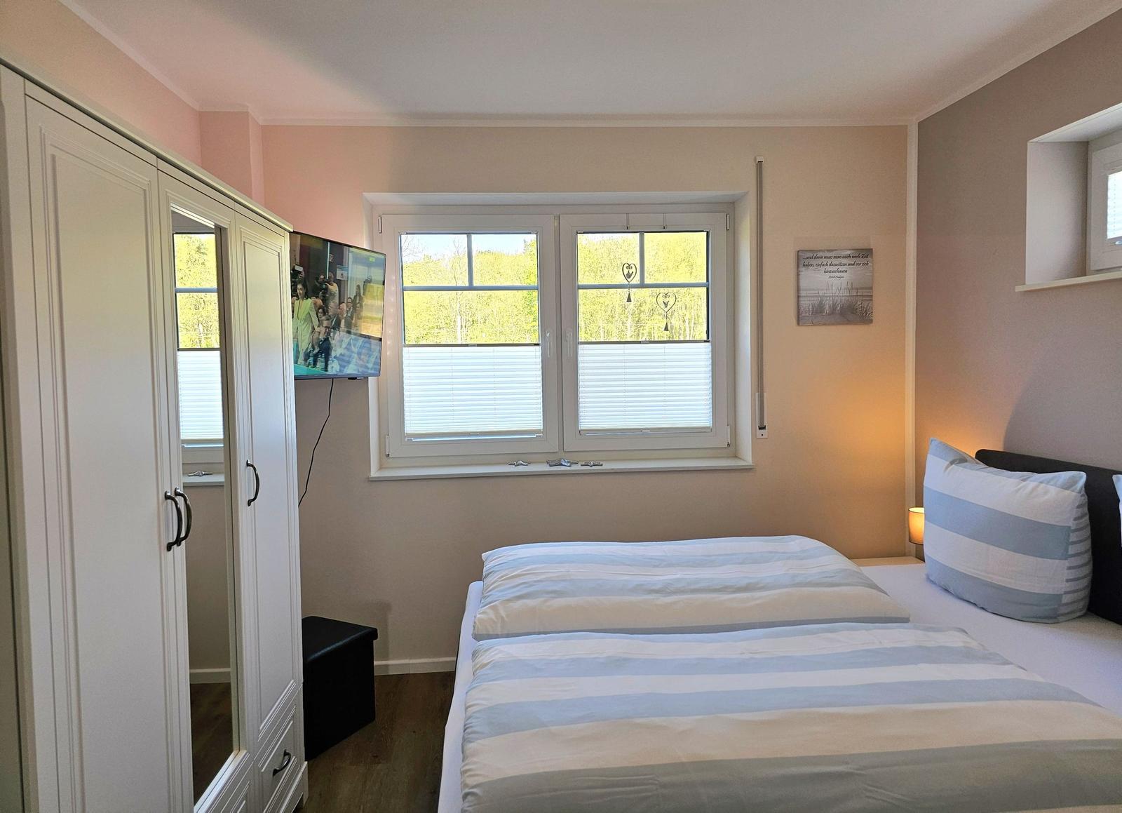 Schlafzimmer mit Doppelbett, Fenster und Kleiderschrank.