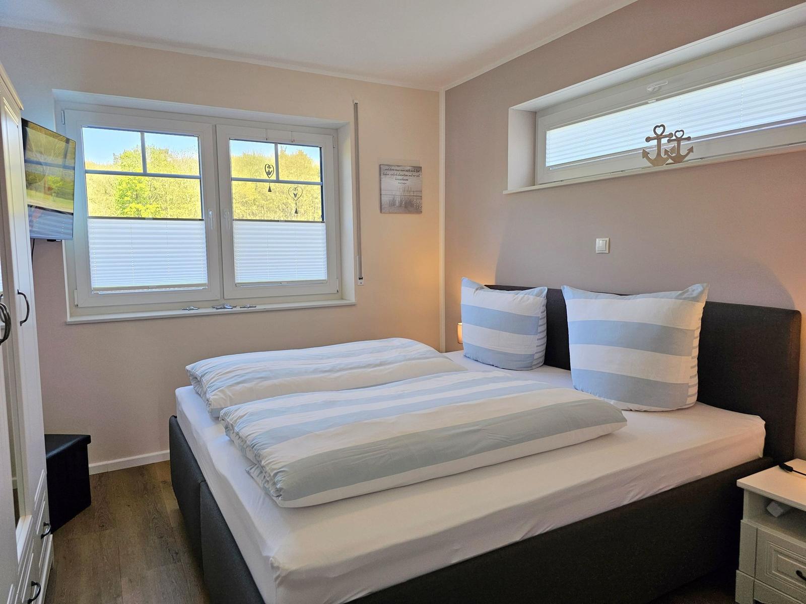 Schlafzimmer mit Bett, Fenstern und TV. Wandbild und Ankerdekoration.