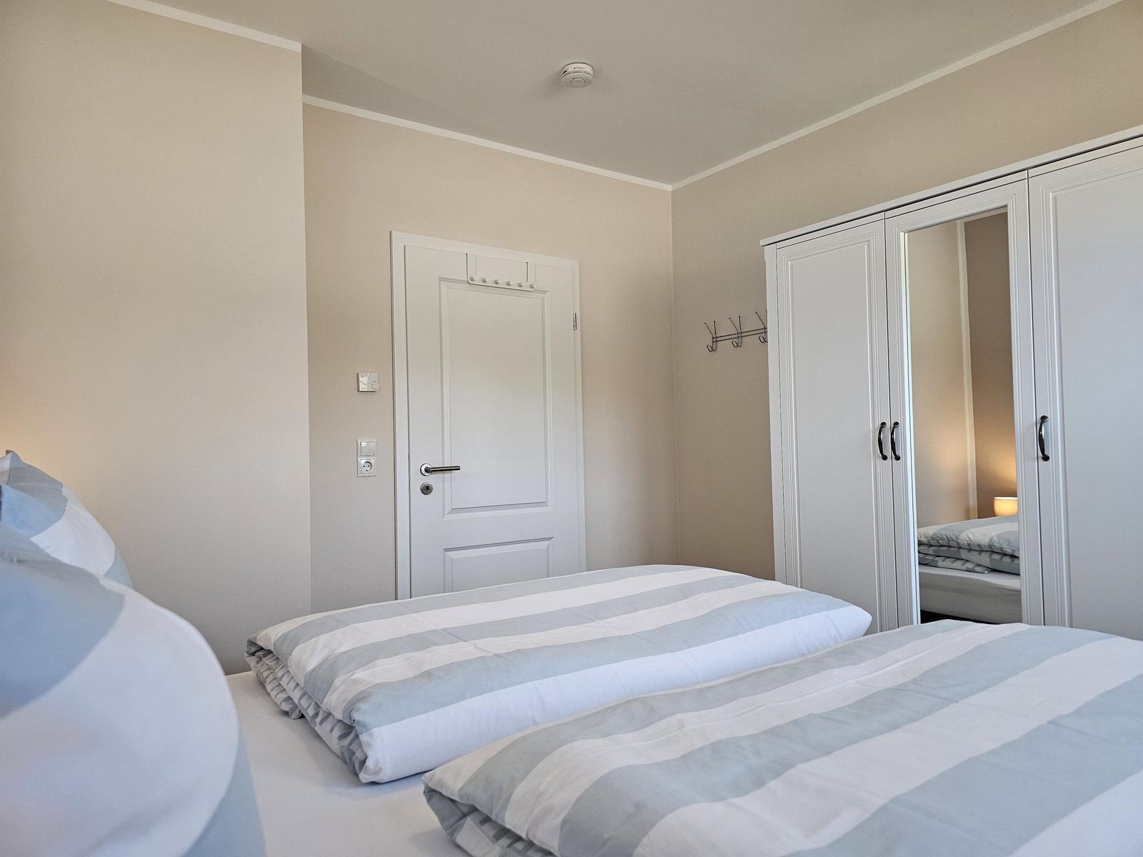 Schlafzimmer mit zwei Betten, Kleiderkabinett und Tür.