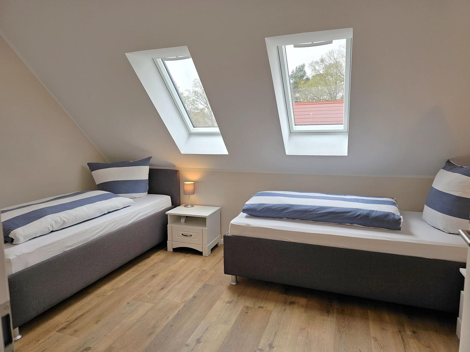 Zwei Einzelbetten mit blau-weißen Bettwäschen, Holzboden und zwei Dachfenster.