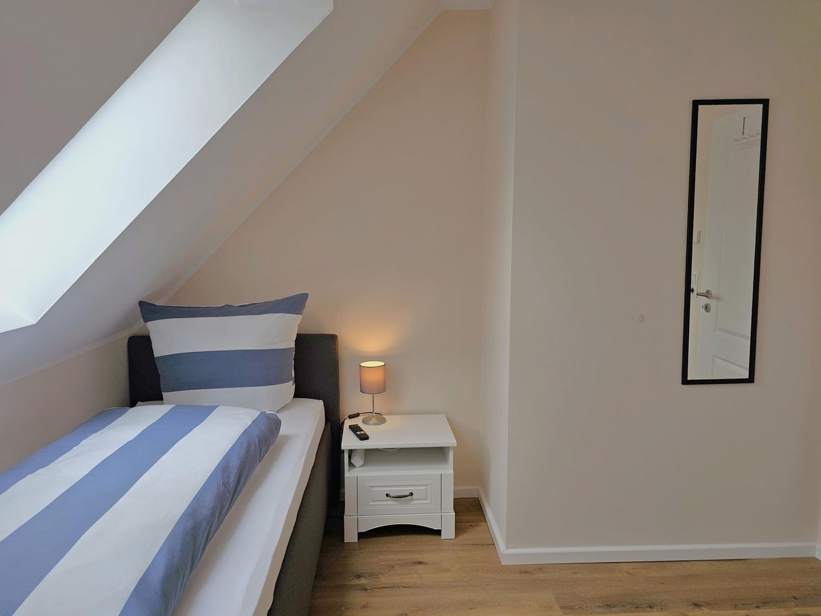 Schlafzimmer mit Dachschrägen, Bett, Nachttisch und Spiegel an der Wand.