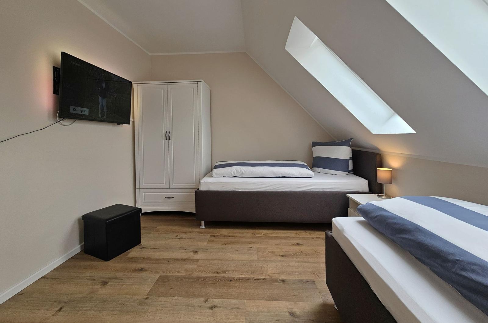 Zwei Betten, Schrank, TV und Dachschrägenfenster in einem Schlafzimmer.