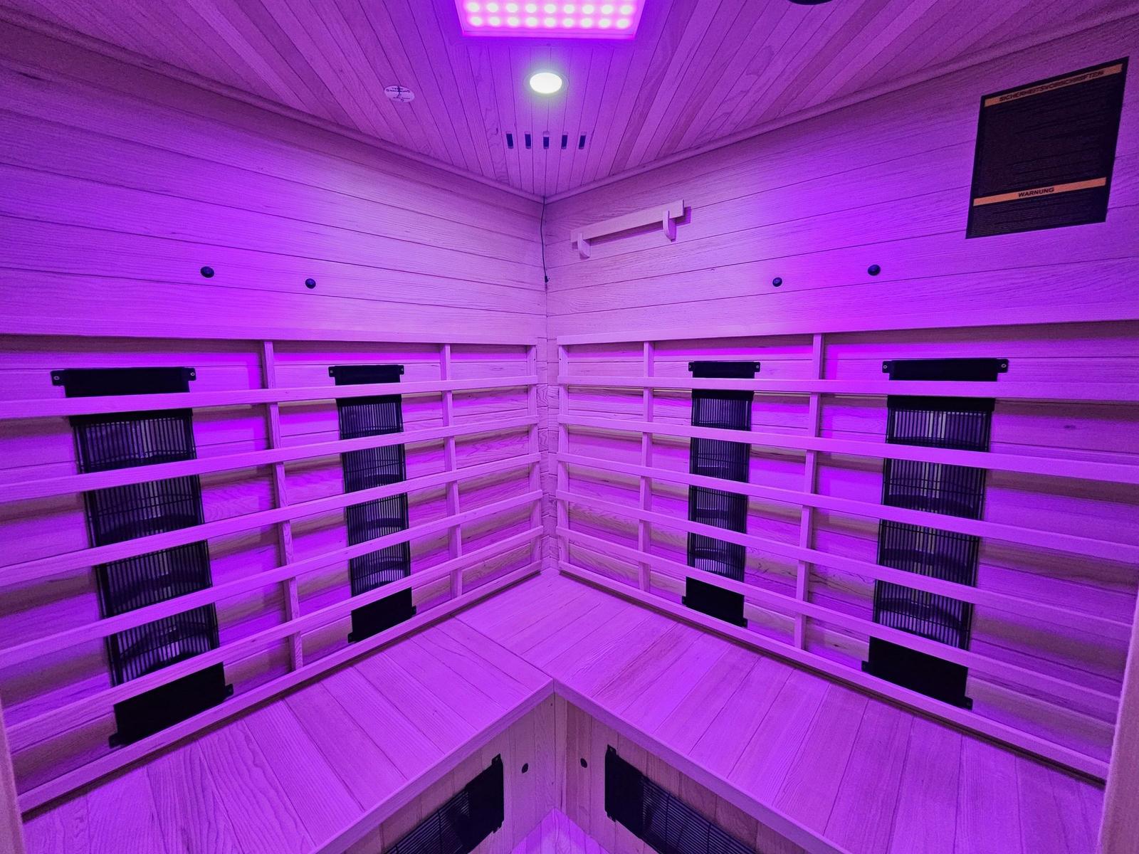 Sauna mit Holzwänden und lila Beleuchtung. An den Wänden sind Heizkörper angebracht.