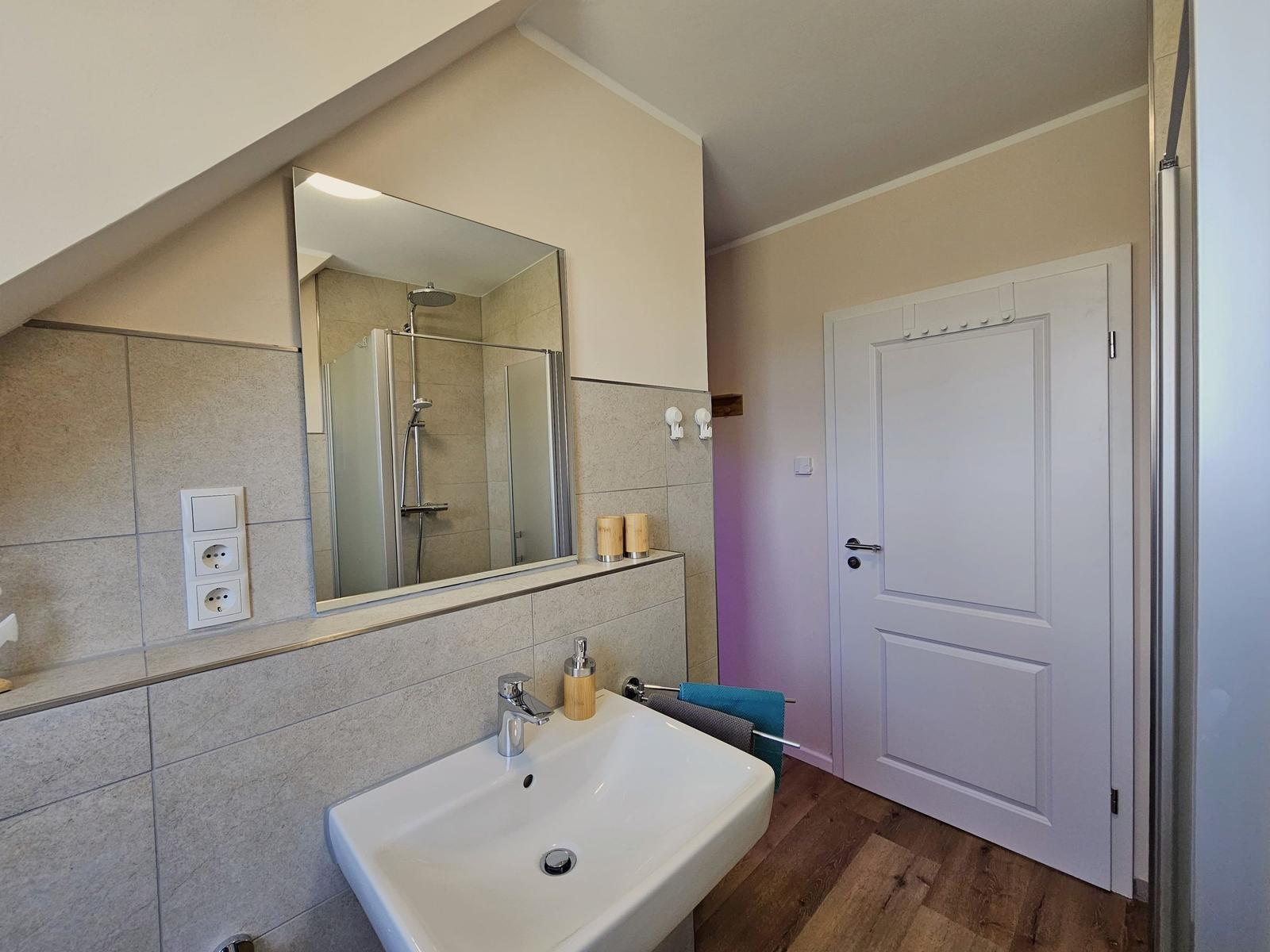 Badezimmer mit Dusche, Waschbecken und Spiegel unter Dachschräge