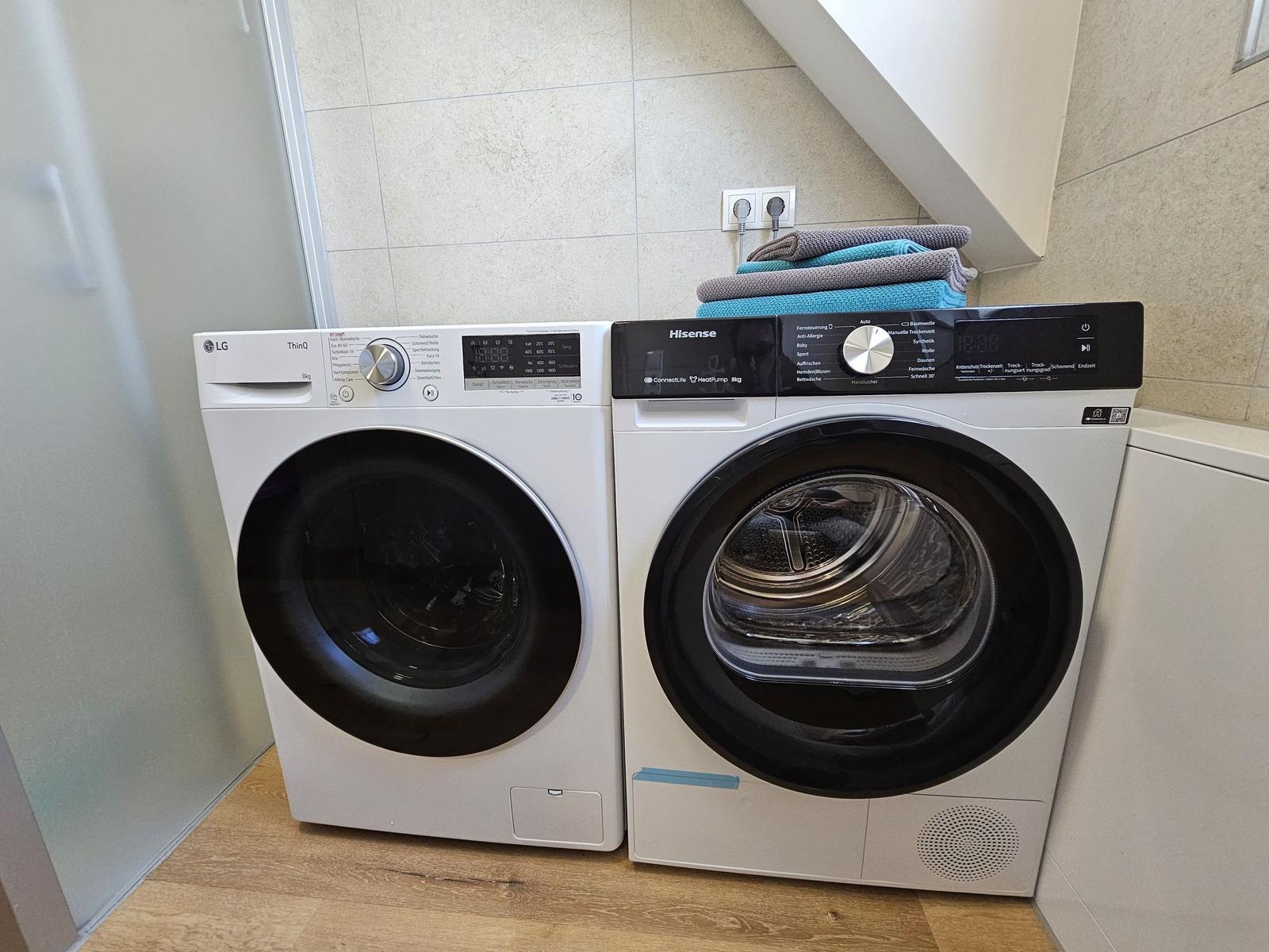 Waschmaschine und Trockner in einem Raum mit Holzboden und Wandbeleuchtung.